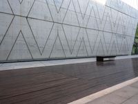 a bench is on the wooden floor in front of a large concrete wall at the park