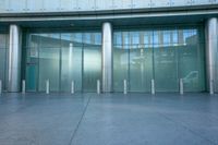 the glass doors of an entrance have white pillars on them and are decorated with stainless poles