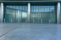 the glass doors of an entrance have white pillars on them and are decorated with stainless poles