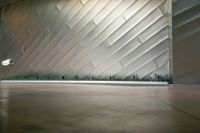 two people walking past a large wall in a building with silver tiles and plants on the side