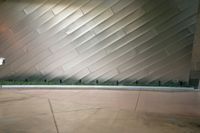 two people walking past a large wall in a building with silver tiles and plants on the side