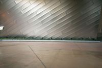 two people walking past a large wall in a building with silver tiles and plants on the side