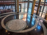 a circular marble floor in front of tall windows in a large building with a clock