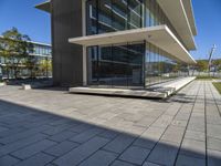 an empty bench in front of a glassed building outside a city center area with benches and trees