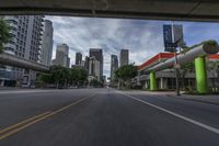 a view from a motorcycle on an open street with city buildings in the distance while riding under a bridge