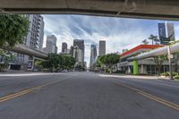 a view from a motorcycle on an open street with city buildings in the distance while riding under a bridge