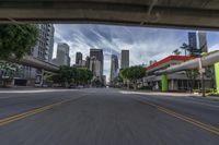 a view from a motorcycle on an open street with city buildings in the distance while riding under a bridge