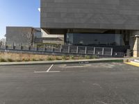 a tall grey building that has multiple windows and steps outside it and a car in front