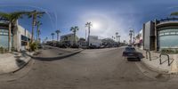 a street with cars parked on the road and palm trees in the background with sun and blue skies above