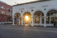 the sun is setting behind a building with columns and arches on it's front