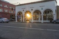 the sun is setting behind a building with columns and arches on it's front