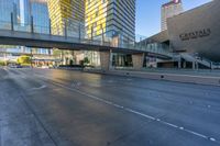 cars driving along on a empty road near tall buildings and a pedestrian crossing over a bridge