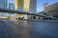 cars driving along on a empty road near tall buildings and a pedestrian crossing over a bridge