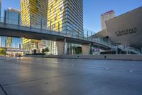 cars driving along on a empty road near tall buildings and a pedestrian crossing over a bridge