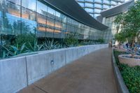 a group of plants in pots line the walls of this building, in front of a glassed - in walkway