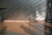 a small fountain and concrete wall in an enclosed room, with sunlight streaming down on it