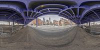 a fisheye lens photo of a city area in front of an overpass and onlookers