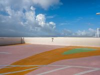 a person walking in an outside tennis court with clouds in the sky behind them and a street light