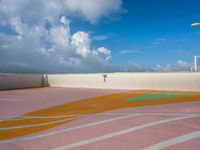 a person walking in an outside tennis court with clouds in the sky behind them and a street light