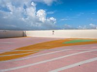 a person walking in an outside tennis court with clouds in the sky behind them and a street light