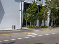 an empty street with parked cars near some tall buildings and trees in front of it