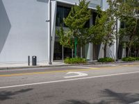 an empty street with parked cars near some tall buildings and trees in front of it