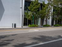 an empty street with parked cars near some tall buildings and trees in front of it