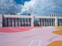 a bright painted court outside a building with lots of windows and pink paint on the ground