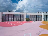 a bright painted court outside a building with lots of windows and pink paint on the ground