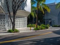 an empty street with a palm tree near a building with geometric patterns on it and two people