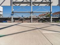 an empty parking lot with buildings in the background and overhead metal and wood structures that frame a bridge