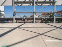 an empty parking lot with buildings in the background and overhead metal and wood structures that frame a bridge