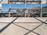 an empty parking lot with buildings in the background and overhead metal and wood structures that frame a bridge