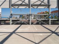 an empty parking lot with buildings in the background and overhead metal and wood structures that frame a bridge