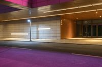 a city bus is traveling down the street under a pink light in a building near a curb