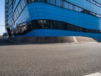 a person with a skateboard riding down an asphalt road by a building made of many smaller glass windows