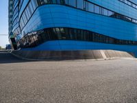 a person with a skateboard riding down an asphalt road by a building made of many smaller glass windows