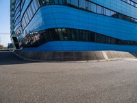 a person with a skateboard riding down an asphalt road by a building made of many smaller glass windows