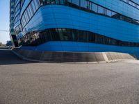 a person with a skateboard riding down an asphalt road by a building made of many smaller glass windows