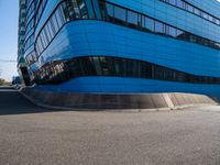 a person with a skateboard riding down an asphalt road by a building made of many smaller glass windows