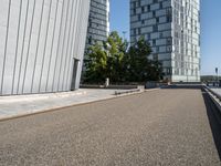 skateboarder in the middle of an urban park near tall buildings with green trees on one side and gray building