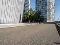 skateboarder in the middle of an urban park near tall buildings with green trees on one side and gray building