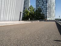 skateboarder in the middle of an urban park near tall buildings with green trees on one side and gray building