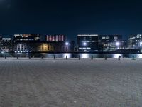 a group of benches sitting on the side of a lake next to some buildings at night