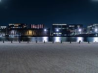 a group of benches sitting on the side of a lake next to some buildings at night