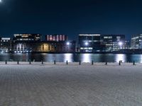 a group of benches sitting on the side of a lake next to some buildings at night