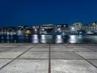 a city by the water is lit up at night time with no clouds in the sky