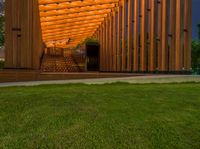 a wooden walkway that leads to a pavilion surrounded by lawn space and stairs in the evening