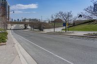 a street near a highway with buildings in the background on a sunny day from the sidewalk