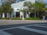 a man crossing the street with his skateboard, in front of the dojo building